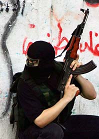 En maskerad Hamas-soldat  gömmer sig bakom en husvägg i staden Gaza City. Foto: Eyad Albaba/PrB