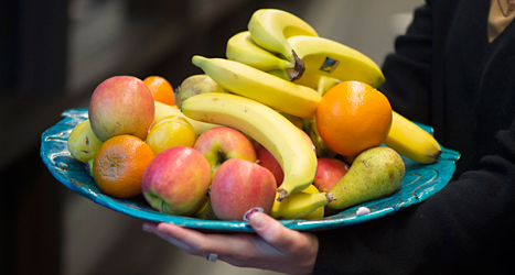 En person håller i ett stort fat med bananer, äpplen och apelsiner