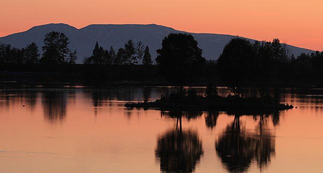 En rosa himmel syns bakom fjället och speglar sig i en blank sjö