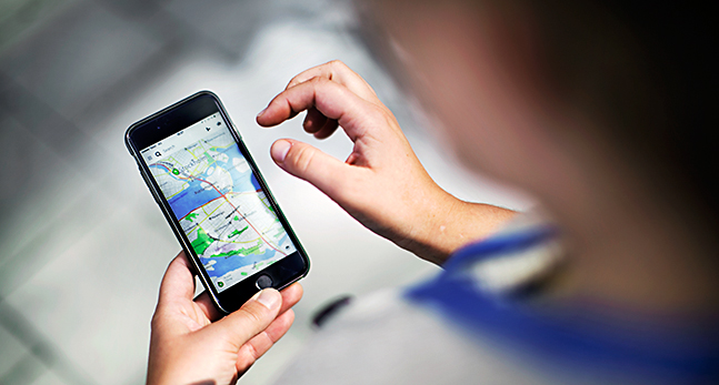 En person håller i en mobil. Man ser en karta på mobilen och personens två händer.