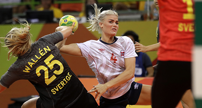 En norsk spelare med bollen tränger sig emellan två svenska spelare