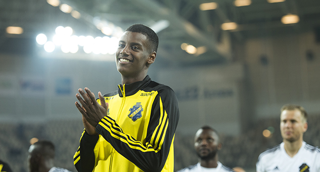 Alexander Isak i AIKs träningsjacka står på planen och klappar händer. Han ser glad ut.