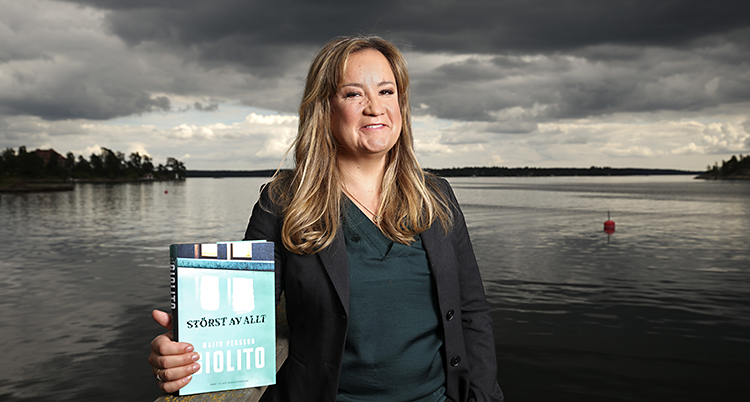 Malin Persson Giolito i grön blus och svart kavaj står framför ett hav i skymningen.