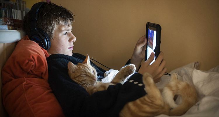 En kille ligger i en säng och tittar på en film i en iPad.