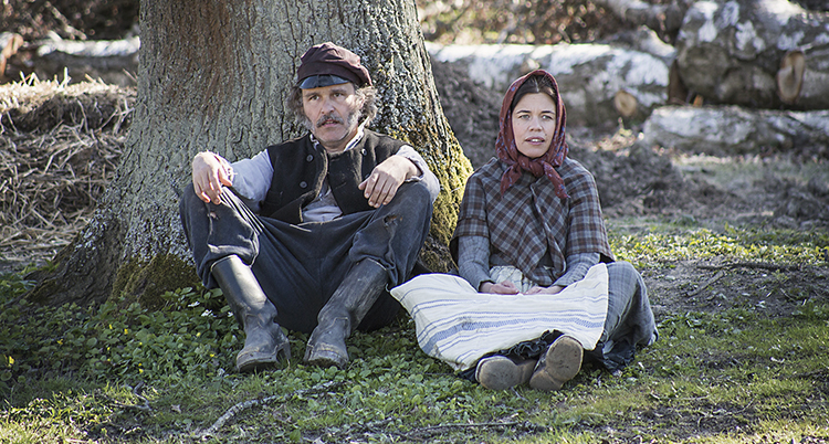 De två programledarna har gammeldags kläder och sitter på marken.