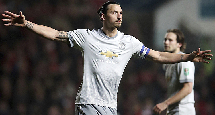 Zlatan på fotbollsplanen. Han har vita kläder och sträcker ut armarna i en vinnande gest.