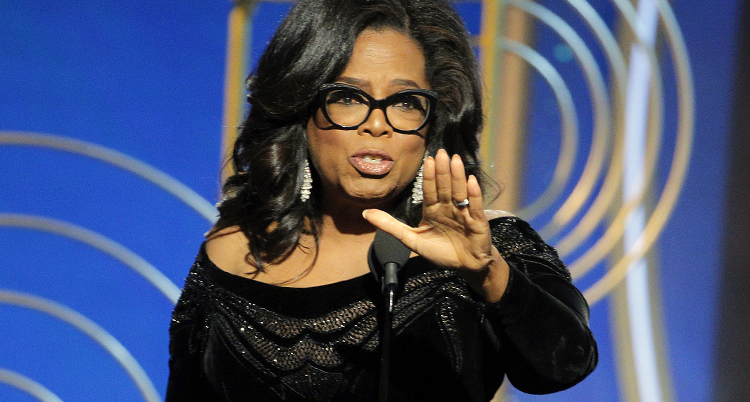 Oprah Winfrey pratar i en mikrofon och håller fram handen.
