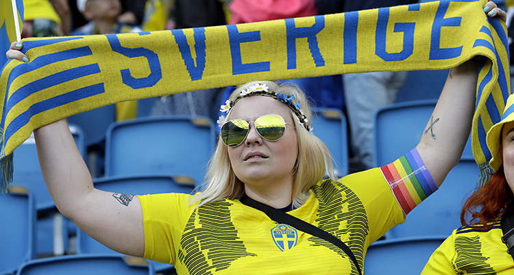 En kvinnlig supporter i svensk tröja håller upp en halsduk det står Sverige på.