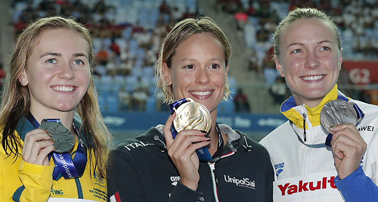 Tre simmare håller upp sina medaljer efter ett lopp.