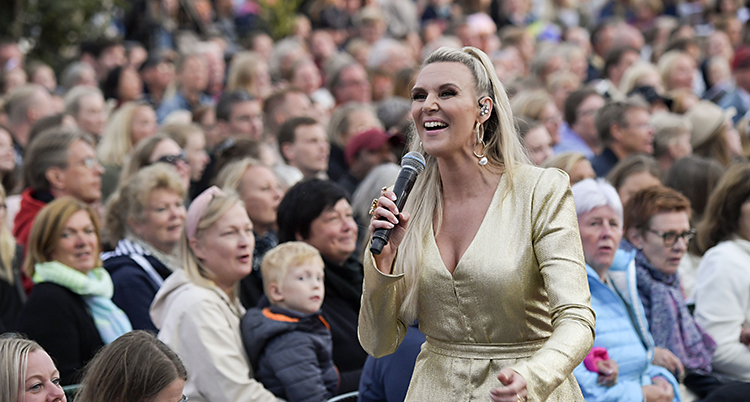 Sanna ler och sjunger. Masor av folk i bakgrunden.