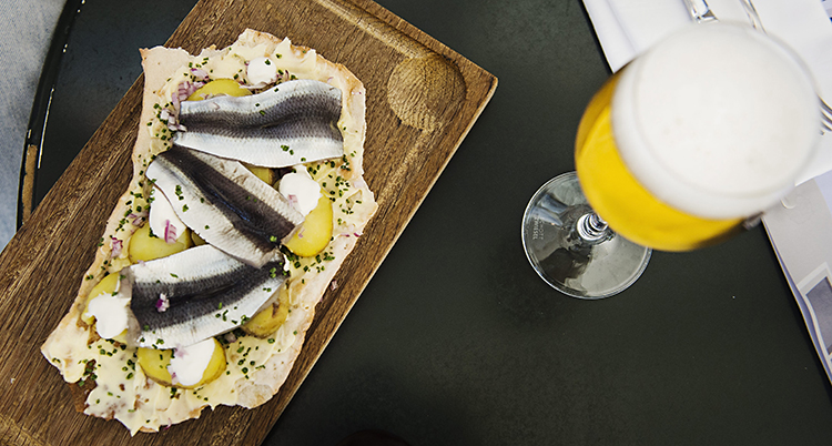 En bricka med en tunnbrödmacka med potatis och strömming. Vid sidan om står ett glas öl.