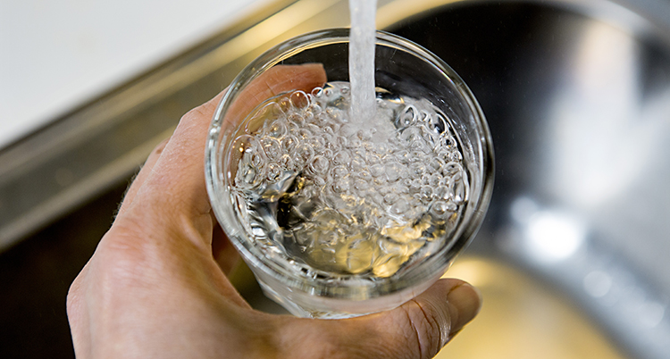 En hand håller i ett glas under en kran. Vatten rinner ner i glaset.