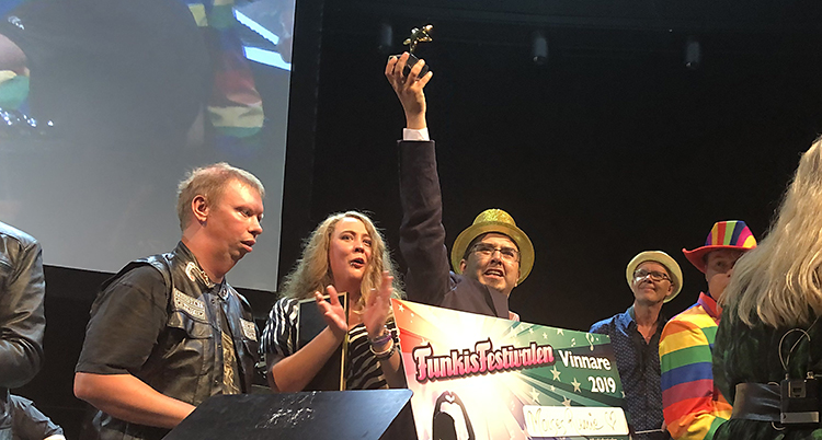 Flera personer står på en scen. Moises Rumie har en hatt och sträcker upp sitt pris i luften.