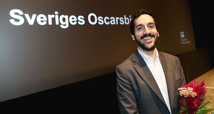 En glad regissör framför en vägg där det står Sveriges Oscarsbidrag.
