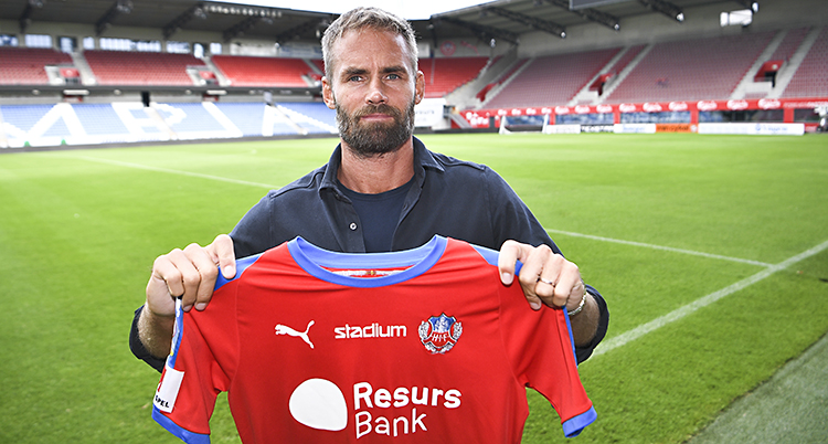 Olof Mellberg står på arenan Olympia. Bakom syns gräsmattan och läktaren. Mellberg håller i en röd tröja för Helsingborgs IF.