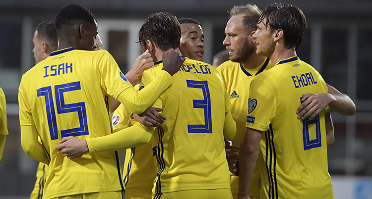 Några spelare i Sveriges landslag i fotboll kramar om varandra efter ett mål. De som står närmast i bilden har ryggen mot kameran. Spelarna har på sig gula tröjor med namn och siffror i blått.