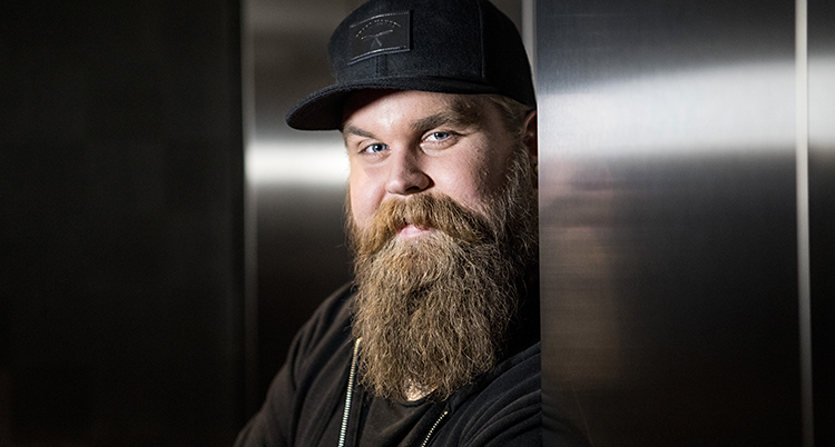 Artisten Chris Kläfford ler mot kameran. Han har ett stort skägg och en svart keps.