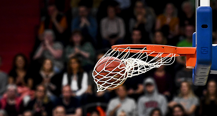 En basketboll som har åkt i en korg. Bollen ligger i nätet som svänger åt sidan. I bakgrunden syns publik.