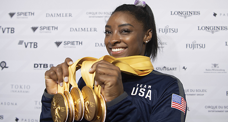 Simone ler och håller upp fem tunga medaljer.