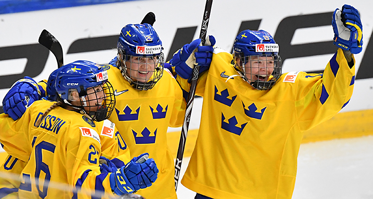 Bilden är från ishockey-VM för damer. Sverige har precis gjort mål. Tre spelare jublar. De har gula tröjor med tre blå kronor på, och blå hjälmar.