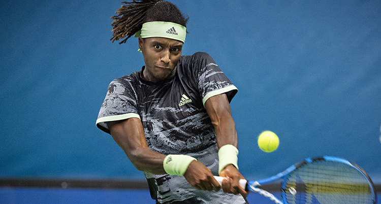 Han har svart hår i dreadlocks och skjuter en gul tennisboll