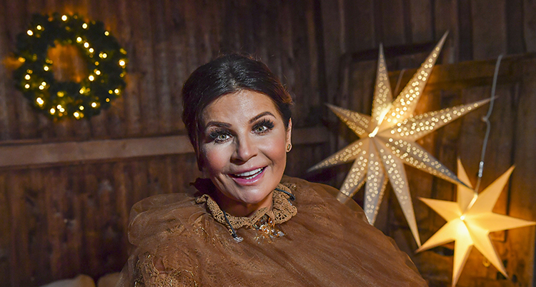 Carola Häggkvist i brunt ler mot kameran. Bakom henne en tänd adventsstjärna.