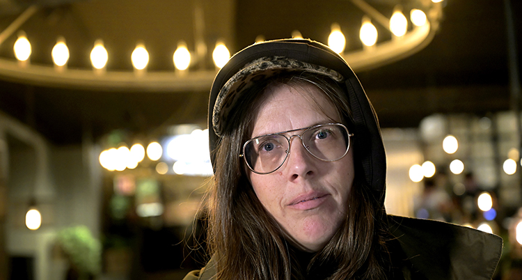 Bild på Sara Olausson. Hon har glasögon och en keps och en luva på huvudet. I bakgrundens syns lampor.