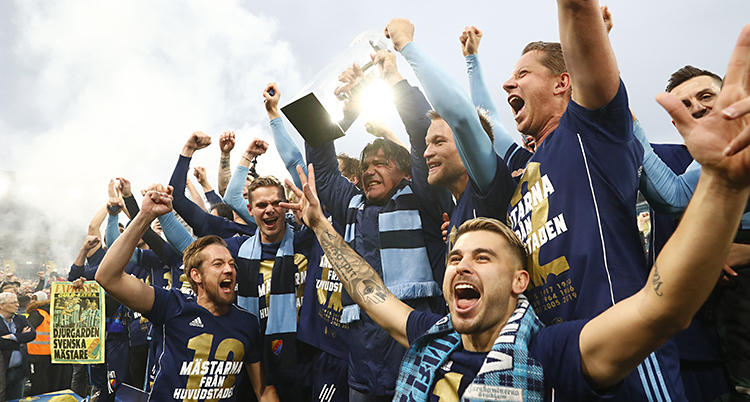 Spelarna sträcker upp armarna och jublar. Spelaren i mitten håller upp på pokalen.