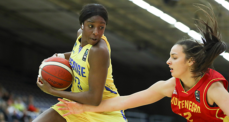Bilden är från en basketmatch mellan Sverige och Montenegro. Sveriges spelare Binta Drammeh håller undan bollen. En spelare från Montenegro försöker ta bollen.