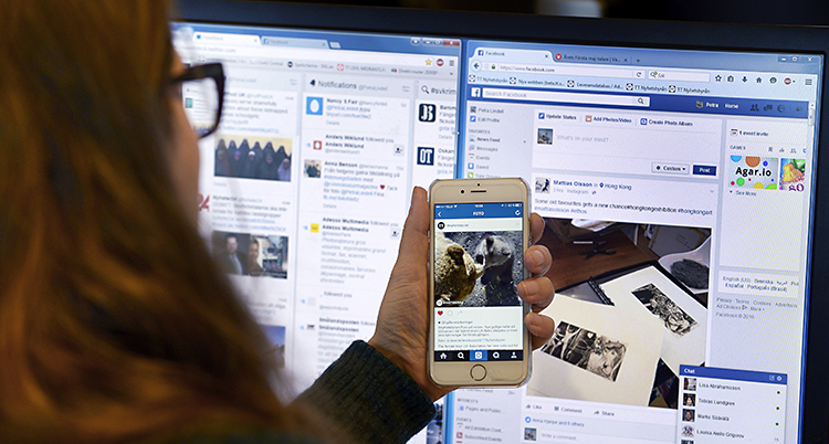 En kvinna sitter framför en dator. I handen håller hon i en mobil. På datorn syns sajten Facebook. Den sajten samlar in mycket information om sina användare.
