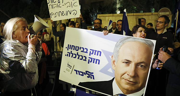 En grupp människor har samlats på en gata. De ropar saker och har plakat. De vill visa sitt stöd till politikern Benjamin Netanyahu.