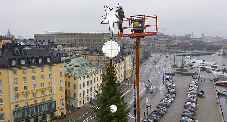 Han står på en hiss högt upp i luften och fixar en stor vit stjärna