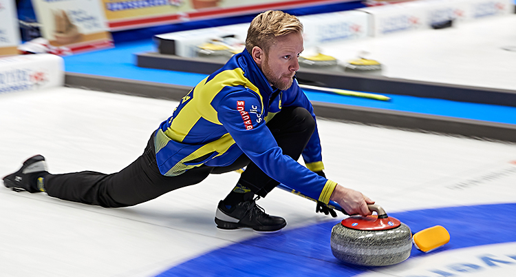 Niklas Edin glider med ett knä i isen och skickar väg en sten.