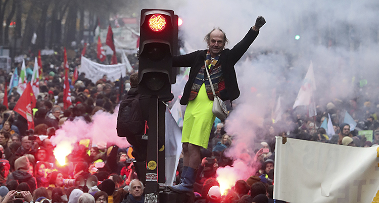 En man har klättrat upp på ett rödljus. Bakom syns ett långt demonstrationståg
