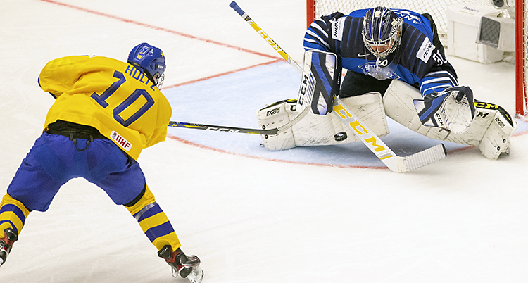 Ryggen på en svensk spelare som skjuter. Pucken är i luften på väg mot målvaktens benskydd.