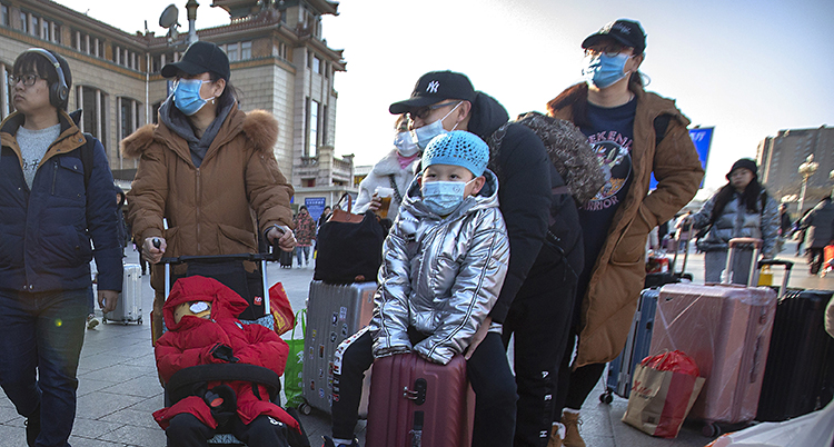 Bilden visar några personer vid en tågstation i Peking i Kina. Personerna har masker för näsa och mun.