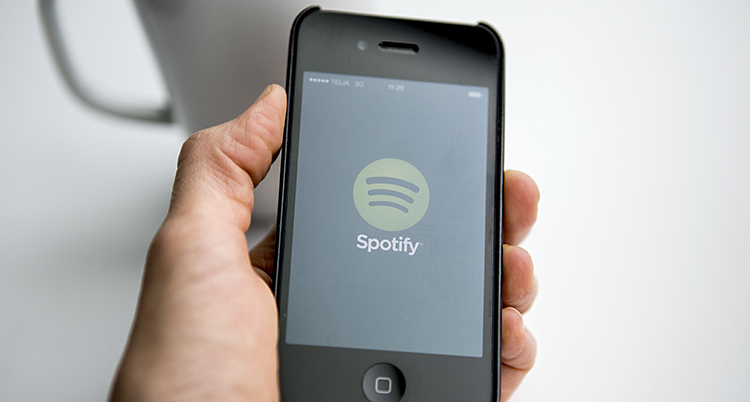 En hand som håller en mobil. På skärmen syns Spotifys logga.