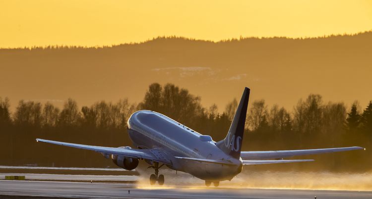 Ett flygplan lyfter från startbanan. I bakgrunden en fantastisk gul-orange himmel. 