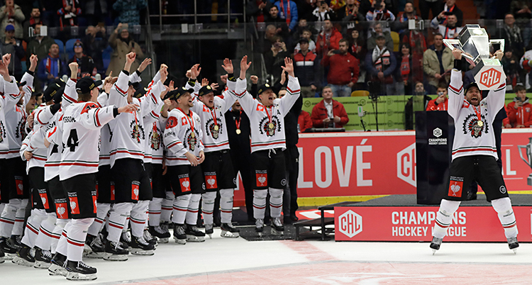 Hela laget Frölunda firar. De står på isen. Spelaren Joel Lundqvist håller upp en pokal i luften. De andra spelarna jublar och sträcker upp händerna i luften.