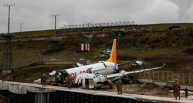 Ett flygplan ligger på marken. Det är trasigt. Några människor står runt flygplanet.