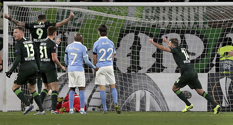 Bilden är från en match i fotboll. Vi ser några spelare i Malmö FF. De har ljusblå tröjor. Spelare i laget Wolfsburg jublar. De har svarta tröjor..