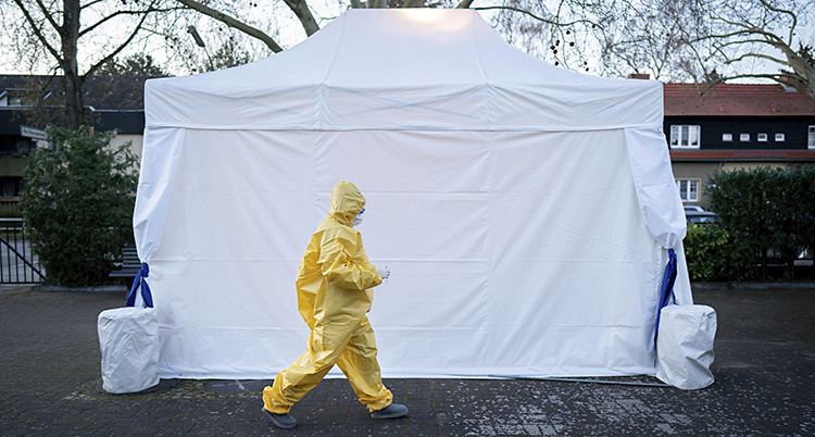 Ett vitt tält syns. Framför det går en läkare i gula skyddskläder.