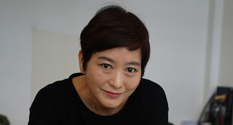 En sydkoreansk kvinna tittar in i kameran. Hon ler. Hon har kort, mörkt hår.