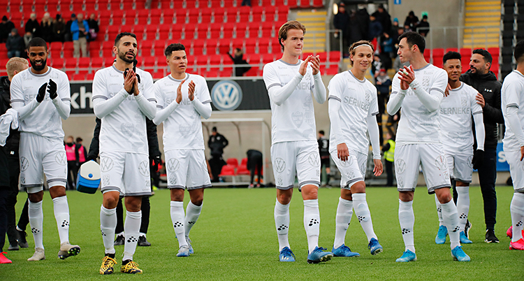 Flera spelare klappar i händerna för att tacka sina fans. De står på en fotbollsplan. De har vita matchkläder.