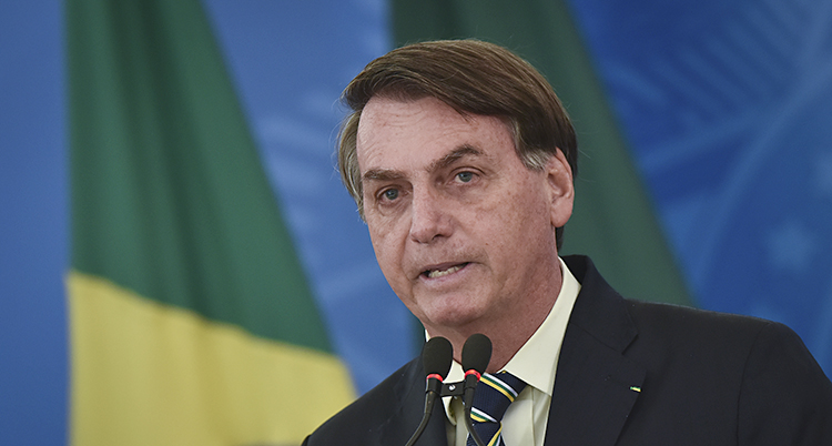 Han pratar i mikrofon framför en brasiliansk flagga