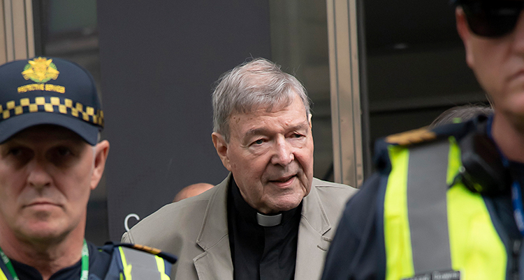 En äldre man är utanför en domstol. På varsin sida om honom syns poliser.