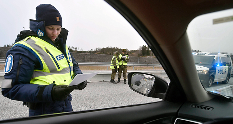 Bilden är tagen inuti en bil. Utanför bilen står en polis och gör en kontroll. Lite längre bort står två andra poliser.
