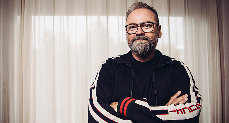 Adam Alsing står med armarna i kors. Han har glasögon och skägg och ser nöjd ut