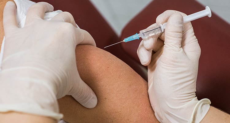 Två händer med handskar sprutar in vaccin i en människas arm