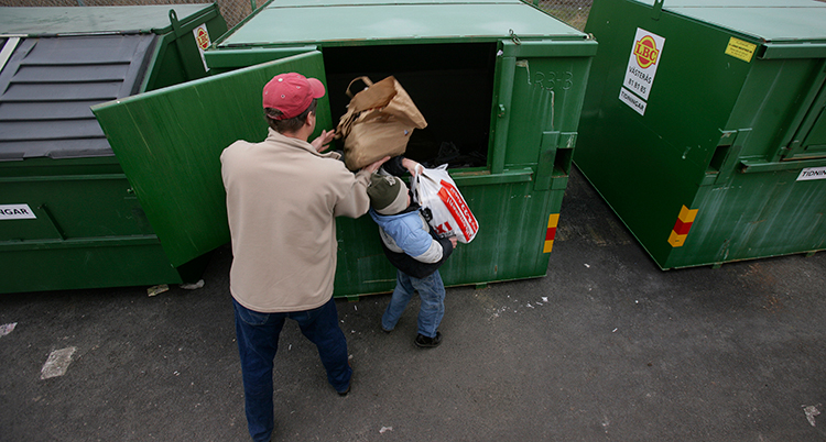 En man och ett barn slänger tidningar i en container.